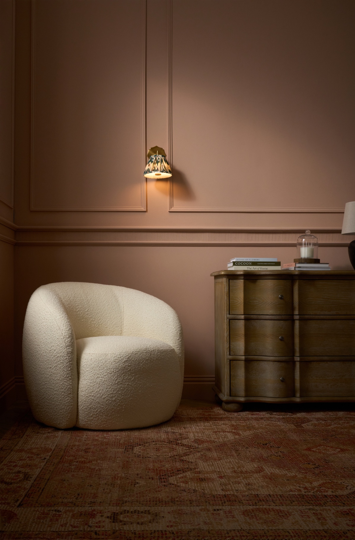 Boucle armchair beside scalloped oak chest in plaster pink room